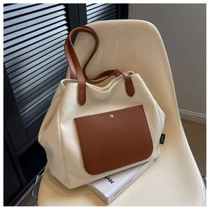 Detail of canvas tote bag showing brown leather pocket and magnetic silver buckle