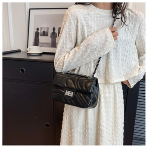 Detail of black quilted crossbody bag with silver twist lock and chain strap on model