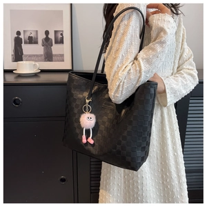 Close-up of black checkered tote bag featuring a cute pink plush charm and logo