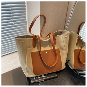 Detail of canvas tote bag with brown leather pocket and dual handles on wooden surface