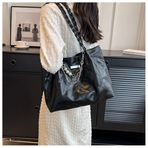 Detail of black woven tote bag featuring quilted patterns, pearl chains, and floral charms