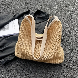 Beige woven straw tote bag with leather straps on urban pavement with magazine