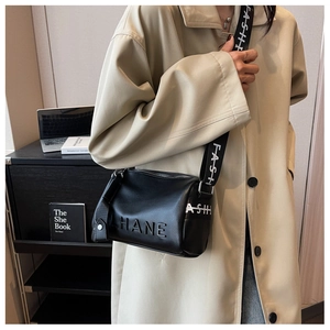Detail of black pebbled leather cylinder bag featuring a contrast lettered shoulder strap