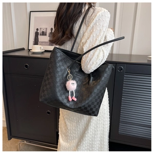 Detail of black checkered tote bag featuring a pink plush monster charm and leather texture