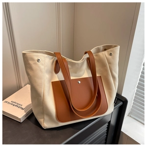 Detail of canvas tote bag showing brown leather handles and pocket on a minimal desk