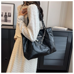 Detail of black quilted tote bag with woven chain strap and pearl floral charms