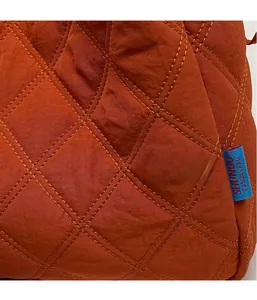 Détail du cabas en toile matelassée orange brûlé avec coutures en losange et étiquette