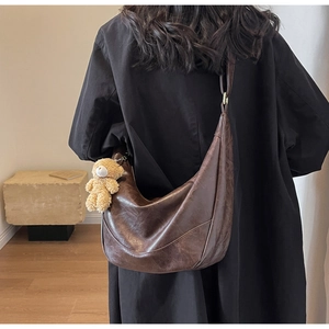 Close-up of vintage brown crescent bag with plush teddy bear charm and leather texture