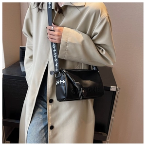 Detail of black crossbody pillow bag with wide textured strap on beige trench coat