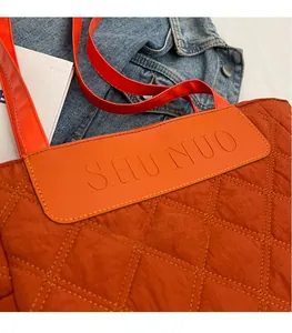 Close-up of caramel orange quilted tote bag featuring a leather logo patch and diamond stitching