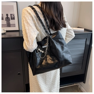 Detail of black quilted tote bag with woven straps and pearl chain accessory