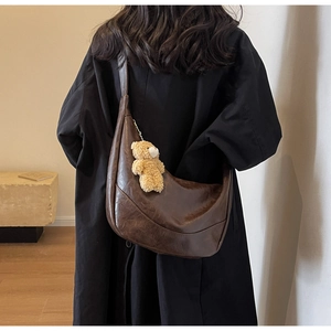 Detail of a dark brown crescent hobo bag with vintage leather texture and plush bear charm