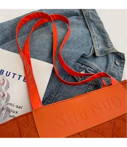 Detail of orange quilted faux leather tote bag with embossed logo and shoulder strap