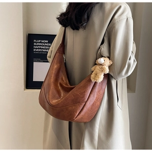 Detail of a large brown hobo bag with vintage texture and a cute plush bear charm