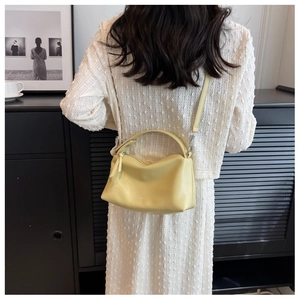 Pale yellow leather shoulder bag with a soft crescent shape shown on a white dress