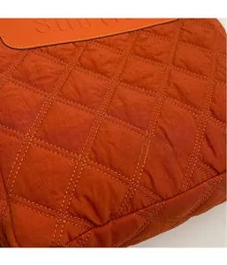 Detailed macro view of orange quilted nylon fabric and leather brand tag on the handbag