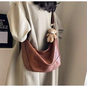 Detail view of caramel faux leather half-moon bag with bear charm and golden buckle