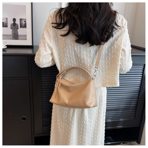 Model wearing a beige Boston style leather shoulder bag over a white textured dress