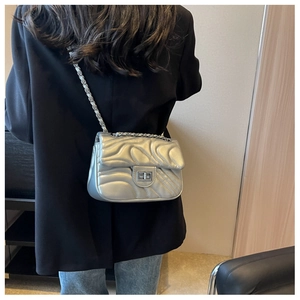 Silver wavy quilted chain bag with metal turn-lock closure on model wearing black blazer