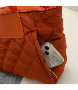 Detail of the orange quilted tote bag featuring a practical side zipper pocket for phone storage