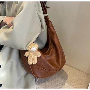 Detail of vintage brown leather hobo bag with a cute plush bear charm for daily use