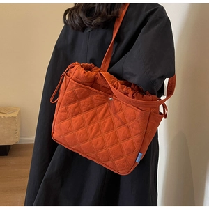 Detail of orange quilted tote bag featuring diamond stitching and drawstring closure