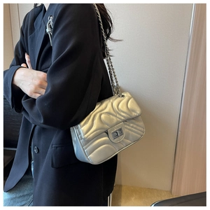 Close-up of silver quilted wave pattern bag with metallic chain and square twist lock