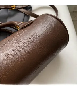 Detailed macro view of dark brown cylinder bag with lychee grain leather and embossed text