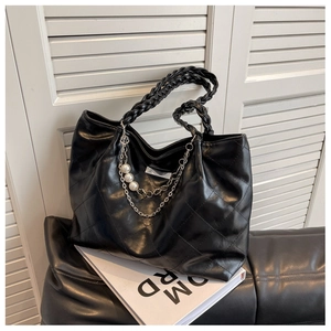 Close-up of black quilted tote bag with woven handle and pearl chain detail