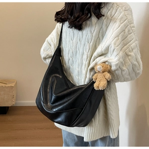 Detail of a black crescent crossbody bag with a plush bear charm and golden zipper