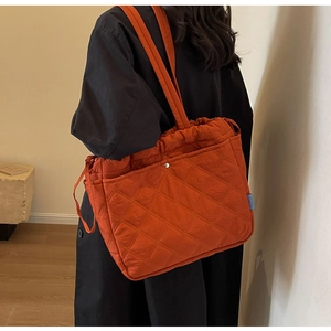 Detail of quilted orange tote bag with diamond stitching worn on shoulder