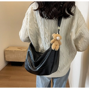 Detail of black leather hobo bag with adjustable wide strap and brown teddy bear charm