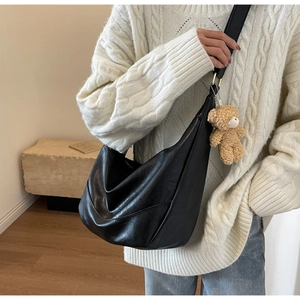 Detail of a large black crescent crossbody bag with a glossy finish and teddy bear charm
