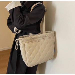 Detail of beige quilted tote bag with drawstring closure and blue side label