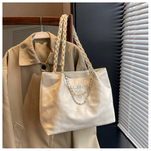 Detail of quilted tote bag with pearl chain accents and woven strap on a wooden hanger