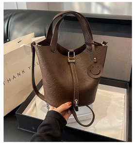 Detail view of brown bucket bag with gold lock and smiley charm in a black gift box