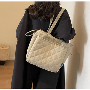 Close-up of beige quilted tote bag with rhombus pattern worn by a model in a minimal setting