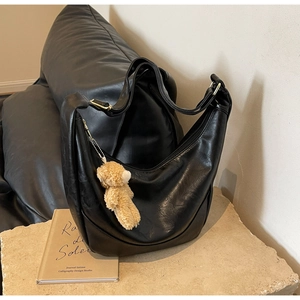 Detail of black large capacity hobo bag with teddy bear charm on stone surface