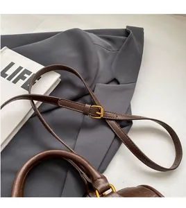 Detail of adjustable deep brown leather shoulder strap with golden metal buckle hardware