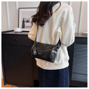 Close-up of black cylinder bag with wide graphic strap worn by a model in a modern interior
