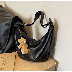 Close-up of black crescent bag on stone base with a cute brown plush bear charm