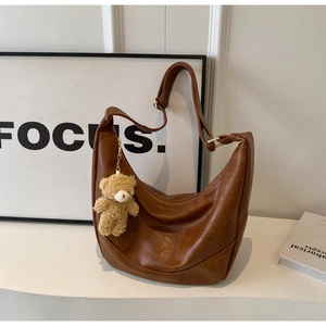Detailed macro of brown leather half-moon bag featuring a plush bear charm and gold hardware
