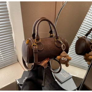 Detail of dark brown Boston barrel bag with brand embossing and cute plush bear charm