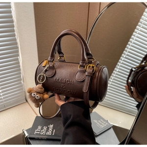 Detailed close-up of brown Boston bag with embossed logo and cute plush bear charm