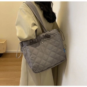 Detail of grey quilted tote bag featuring functional side drawstring and snap button pockets
