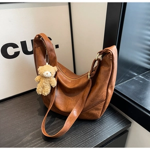Brown semi-circle hobo bag featuring a smooth PU leather texture and a cute plush bear charm
