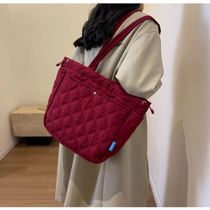 Deep burgundy quilted tote bag with diamond stitching shown on shoulder in daily life