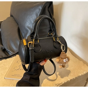 Detail of black Boston cylinder bag with lychee texture and cute monster charm