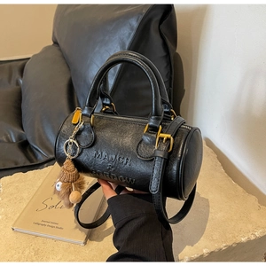 Detail of black Boston cylinder bag with embossed letters and brown plush charm