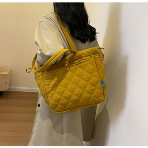 Detail of yellow quilted nylon tote bag featuring diamond pattern and wide shoulder strap